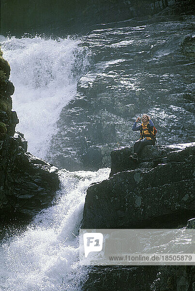 Woman sitting on boulder overlooking waterfall.