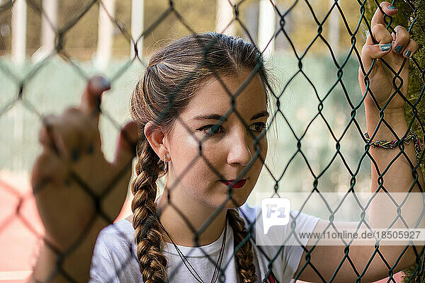 Young woman looks through the bars of a basketball court
