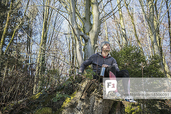 Fit young man relaxing on tree stump in forest