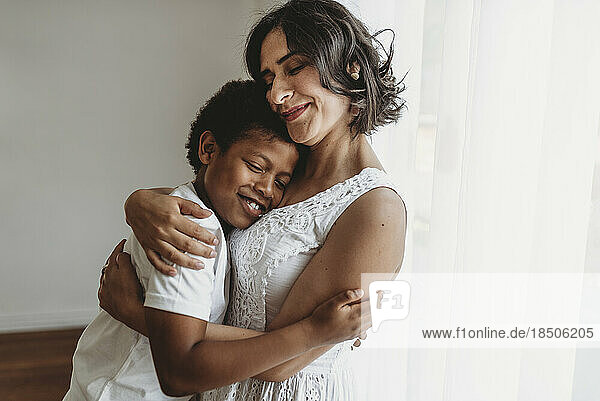 Mother hugging school-aged son in smiling embrace in studio