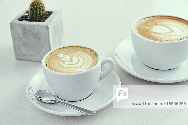 Hot lattes in white coffee mugs on a marble table.