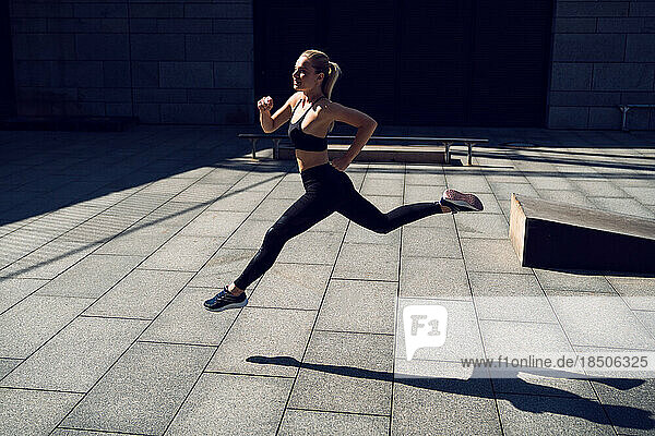 Blondie fit woman in black sportswear running outdoors during workout