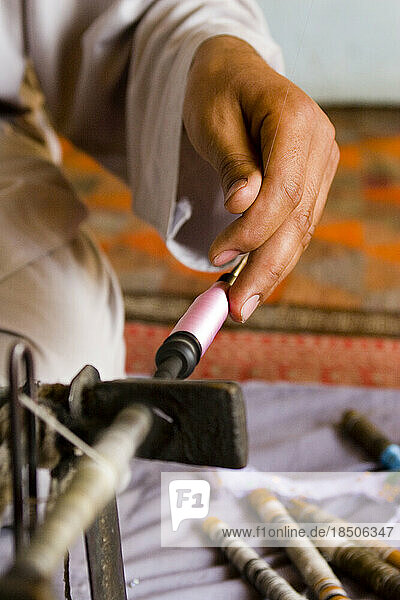 Detail of a hand holding a delicate silk thread on a spinning wheel in Kabul.
