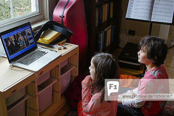 Two children watch Biden inauguration on computer at home