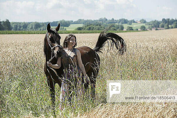 Mature woman standing with her brown horse on wheat field and smiling  Bavaria  Germany