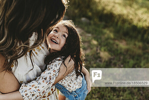 Young happy daughter laughing while being embraced by mother outside