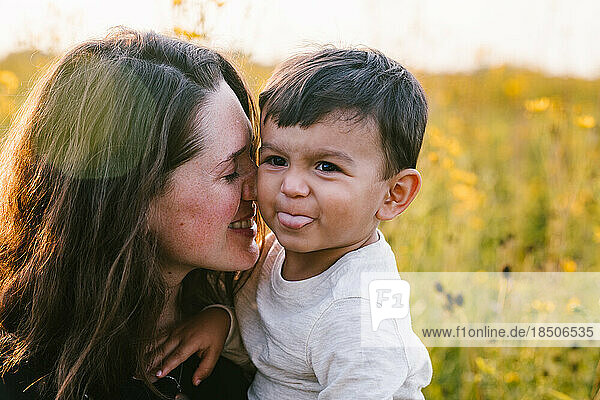 Mother snuggles multiracial son outside in flower field with love