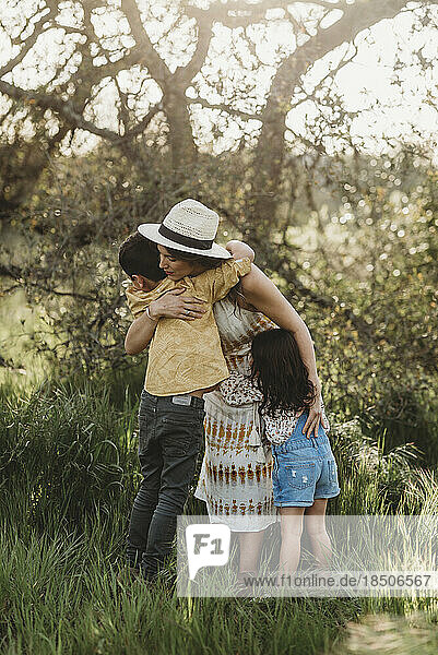 Full length view of mother hugging son and daughter in backlit field