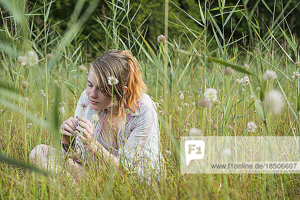 Young woman sitting on meadow and smelling a flower  Bavaria  Germany