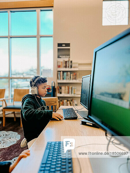 Mixed race kid focusing on computer screen at the library