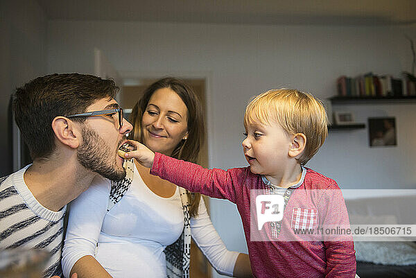 Little boy feeding his father with doughnut while mother is watching  Munich  Germany