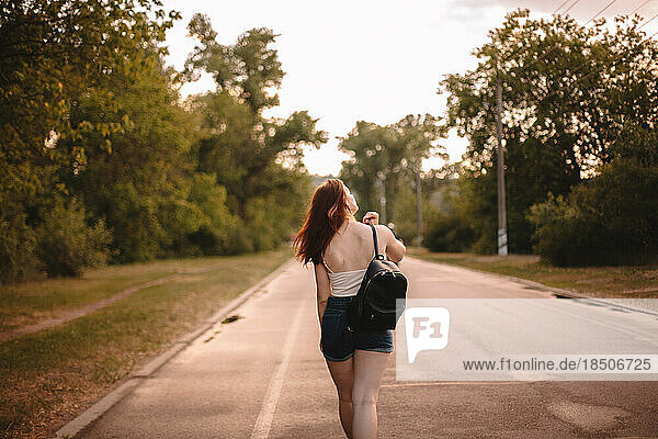 Rear view of young woman walking on country road during summer