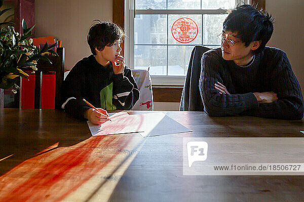 A father sits at table with son working on homework