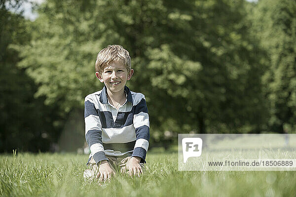 Boy smiling and sitting on a field in park  Munich  Bavaria  Germany