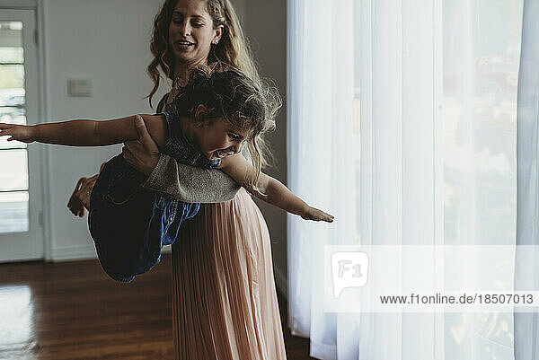 Daughter and mother playing airplane in natural light studio