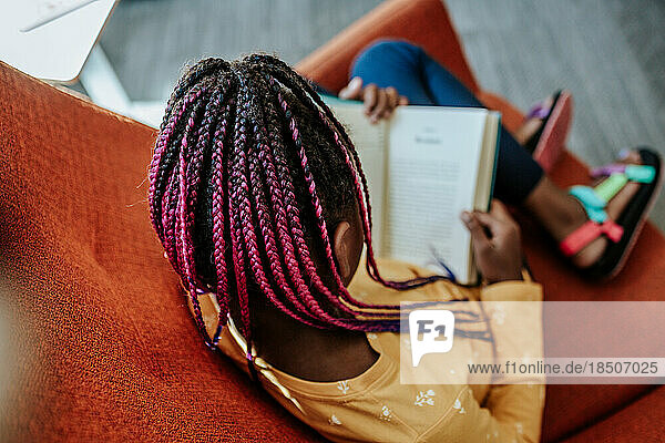 Young African American girl reading a book on an orange chair