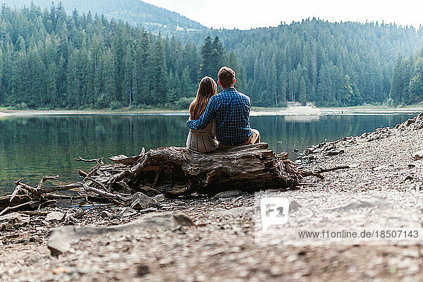 man and a woman are sitting hugging near lake in the mountains