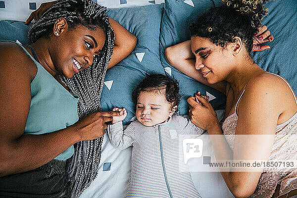 High angle view of loving lesbian mothers holding son's hands while lying on bed at home