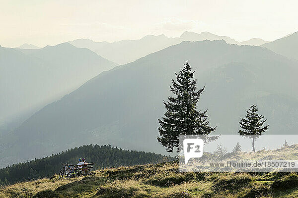 Couple of mountainbikers looking at view and sitting on bench in alpine landscape  Zillertal  Tyrol  Austria