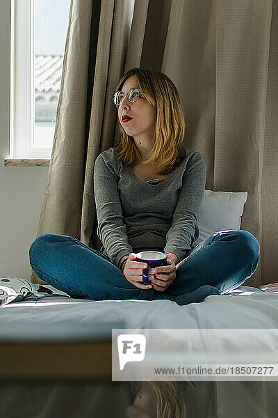 Young woman with a cup of coffee in her bedroom.