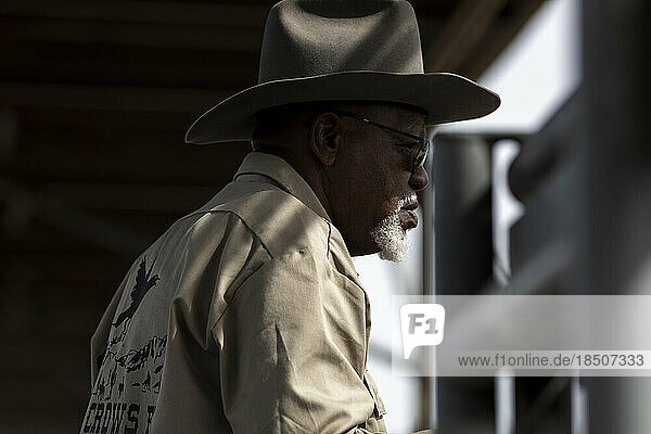A cowboy cast in light and shadow watches the Arizona Black Rodeo