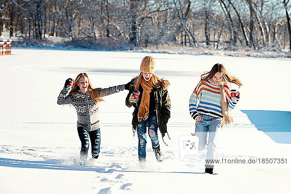 Three tween girls running in the snow on a frozen lake on winter day.