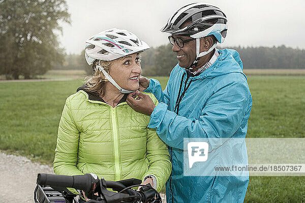 Senior man fastening on bicycle helmet to his wife and smiling  Bavaria  Germany