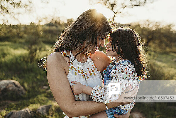 Young mother holding daughter and cuddling in bright california field