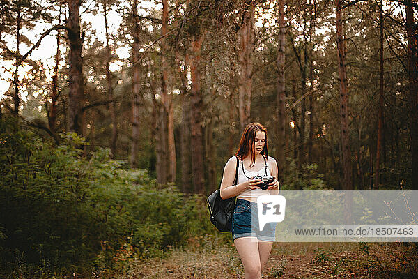 Young woman holding camera while walking in forest
