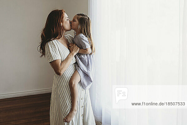 Side view of young mother holding daughter and kissing in studio