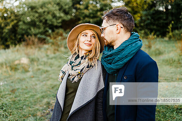 man and a woman in coats are walking through an autumn park on a date