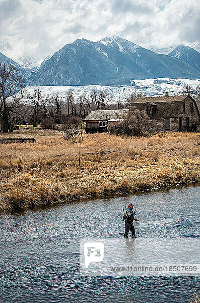 Angler fly fishing in river with snowy peaks in the background