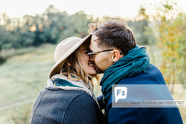 man and a woman in coats kiss in the park on a date