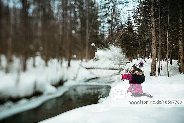 Girl throwing snow in a river on a winter day