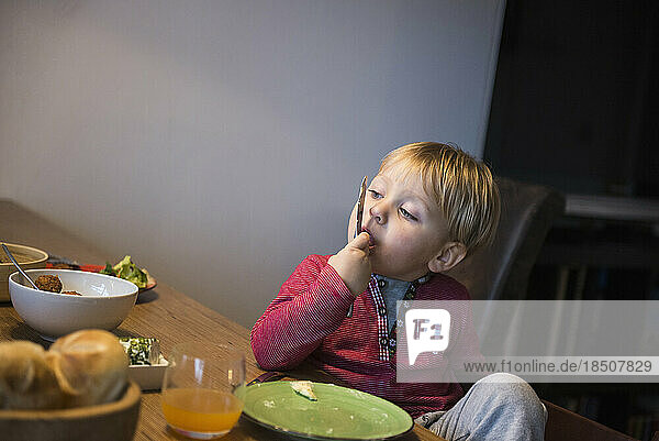Little boy licking his finger at breakfast table  Munich  Germany