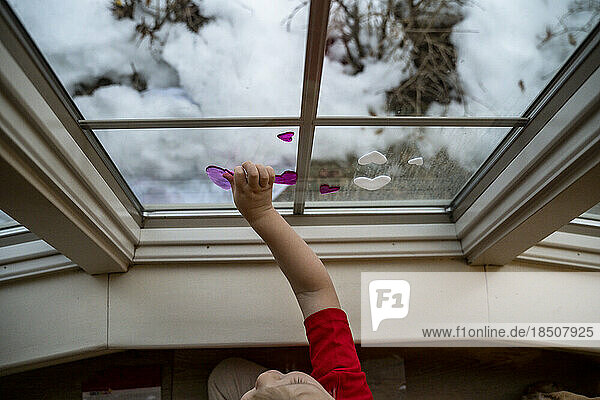 Toddler Boy Placing Window Cling Heart on Window for Valentine's Day