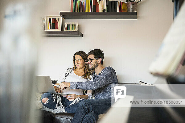 Pregnant woman and husband with laptop on sofa  Munich  Germany