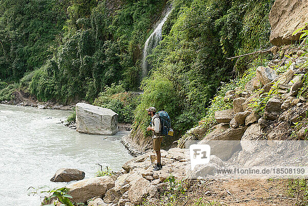 Young man hiking in mountains along river with waterfall