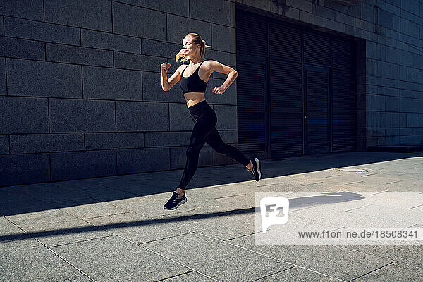 Young and beautiful woman in black sportswear training running