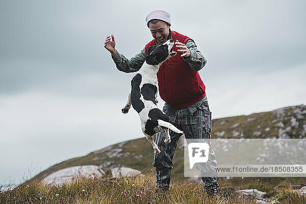 spotty dog jumps in air playing with owner on hill in scotland