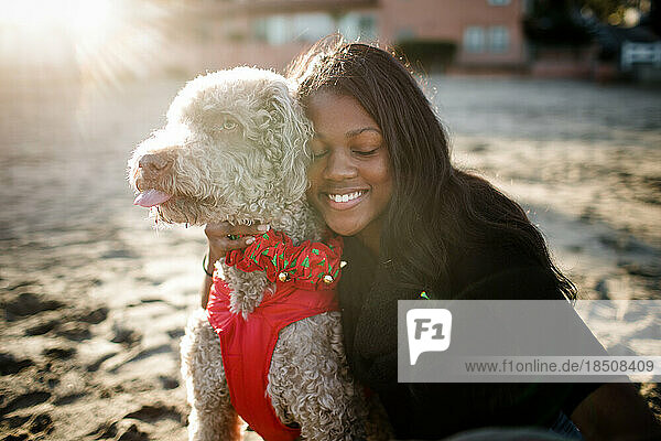 Young girl hugging labradoodle on beach at sunset