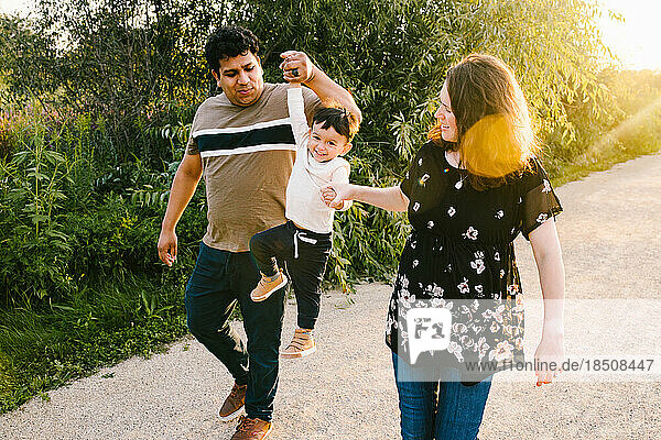 Pregnant mom and latino dad smile and play with son in sunshine