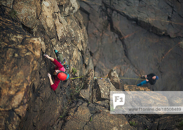 Woman wearing red trad climbing on lead with belayer below