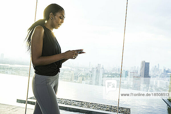 Athletic black woman using her phone outdoors panoramic city view.