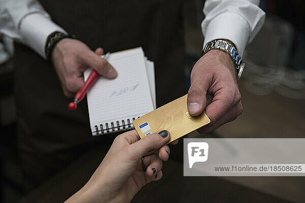Man holding note pad and pen while accepting credit card payment from woman