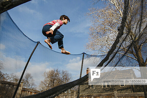 An athletic boy jumps high in trampoline against blue sky