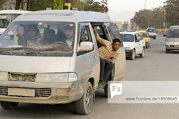 A young man hangs out the open window of a crowded van during rush hour in Kabul.