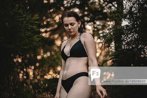 Sensual woman in a bikini standing against trees in forest