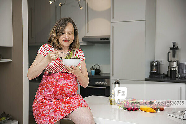 Pregnant woman eating salad in the kitchen  Munich  Bavaria  Germany