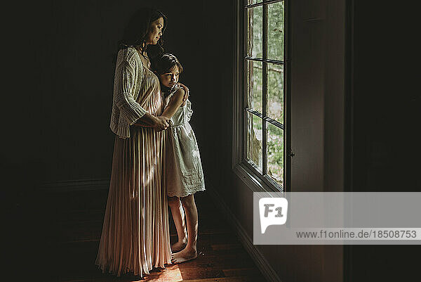 Mother and daughter embrace and looking out studio window